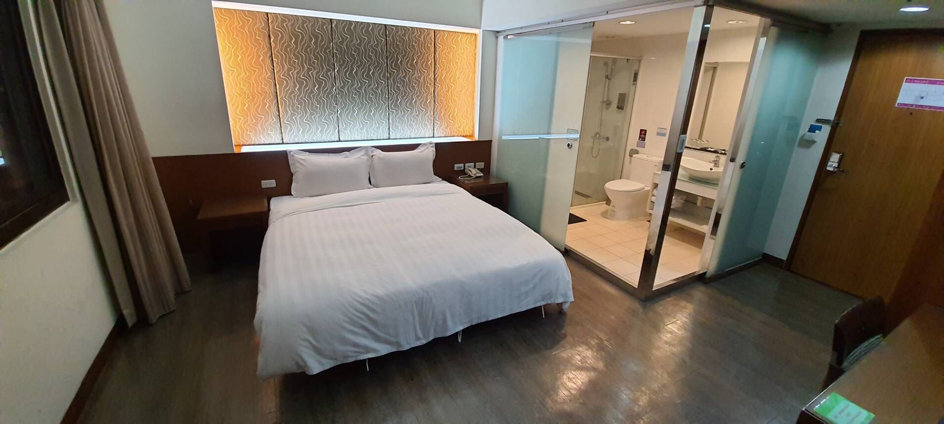Et hotelværelse med seng, et natbord, et spejl, bruseområde og toilet.