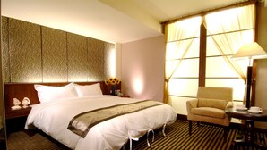 A hotel room with a large bed, a chair, a small table with a lamp, and a window with curtains. - Tapeng Bay Holiday Hotel (Donggang)