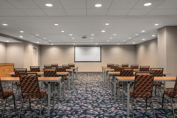 A conference room with a projector screen, multiple tables, chairs, and a carpeted floor.
