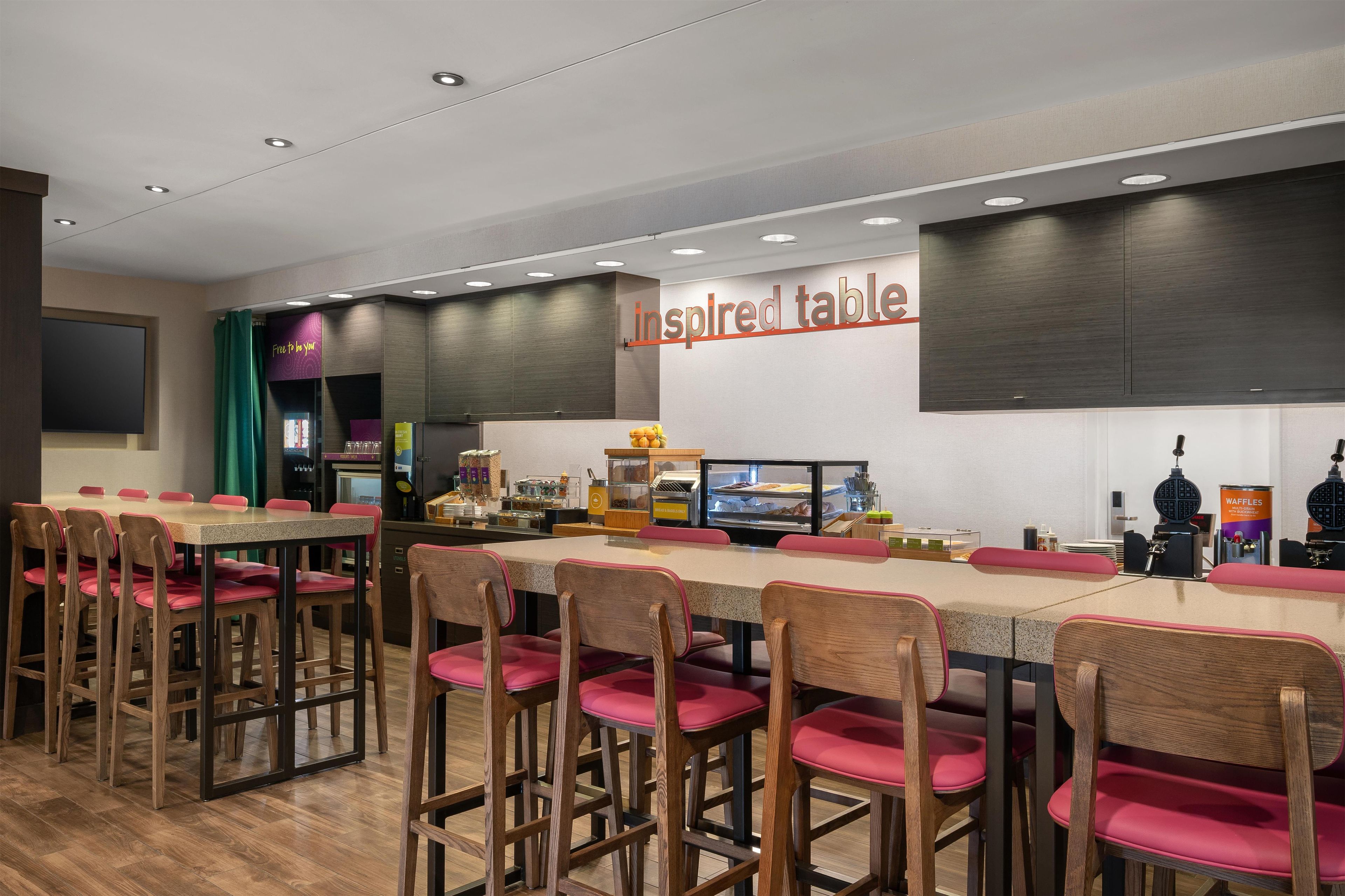 A restaurant with multiple tables and chairs, a self-service beverage station, and a sign reading 'Inspired Table'.