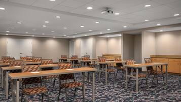 Une salle de conférence dotée de plusieurs tables et chaises, d’un sol recouvert de moquette et d’un plafond pourvu d’un éclairage encastré.