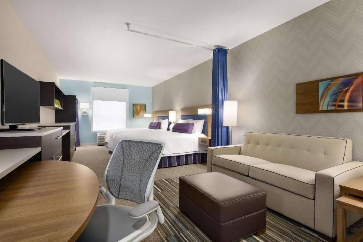 A hotel room with a bed, a sofa, a desk, a chair, and a television.