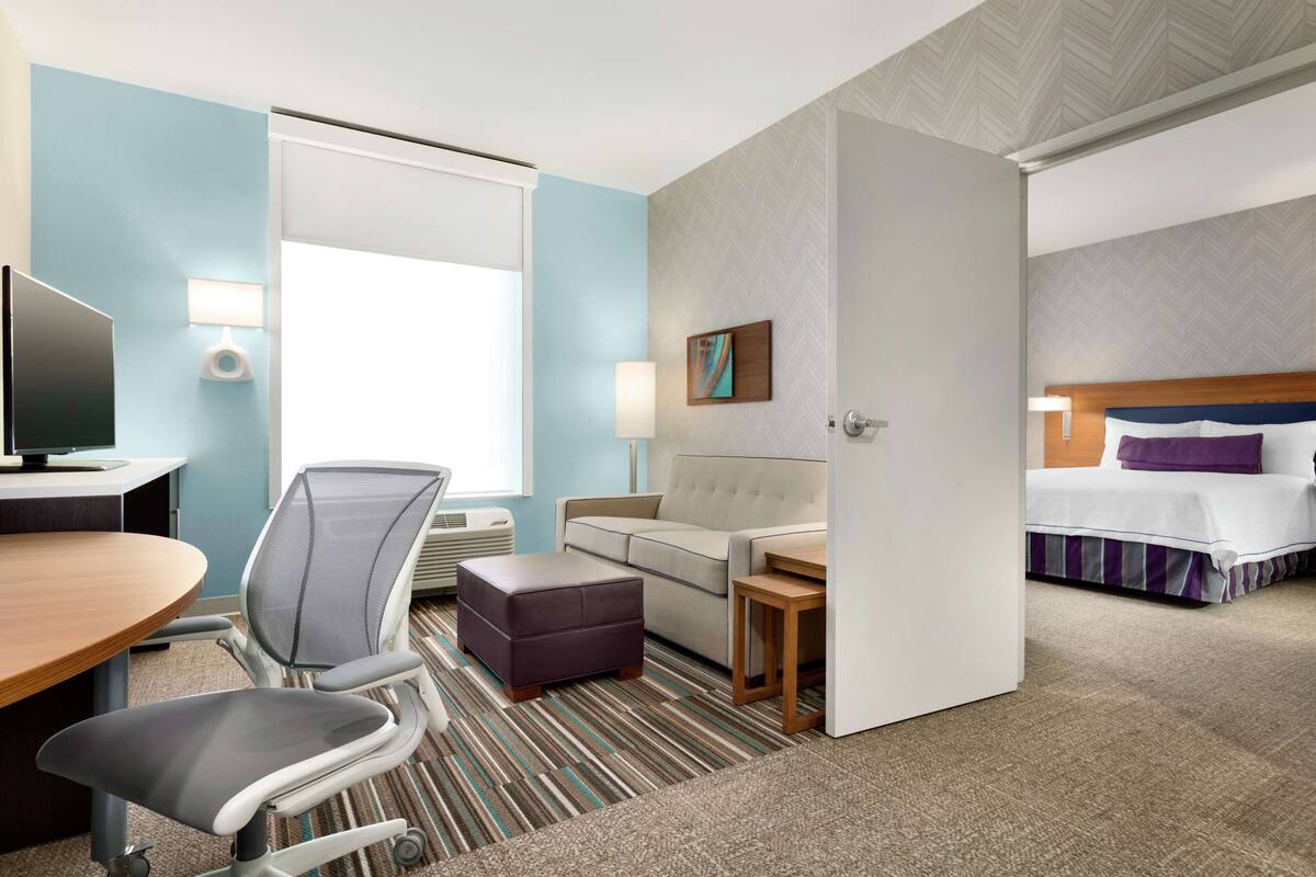 A hotel room with a bed, a sofa, a desk with a computer, a chair, and a small table.