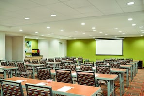 A conference room with multiple tables and chairs, a projector screen, and a green accent wall. - Home2 Suites by Hilton Middletown (Middletown)