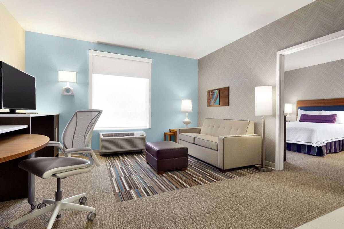 A hotel room with a desk, chair, sofa, ottoman, and a bed.