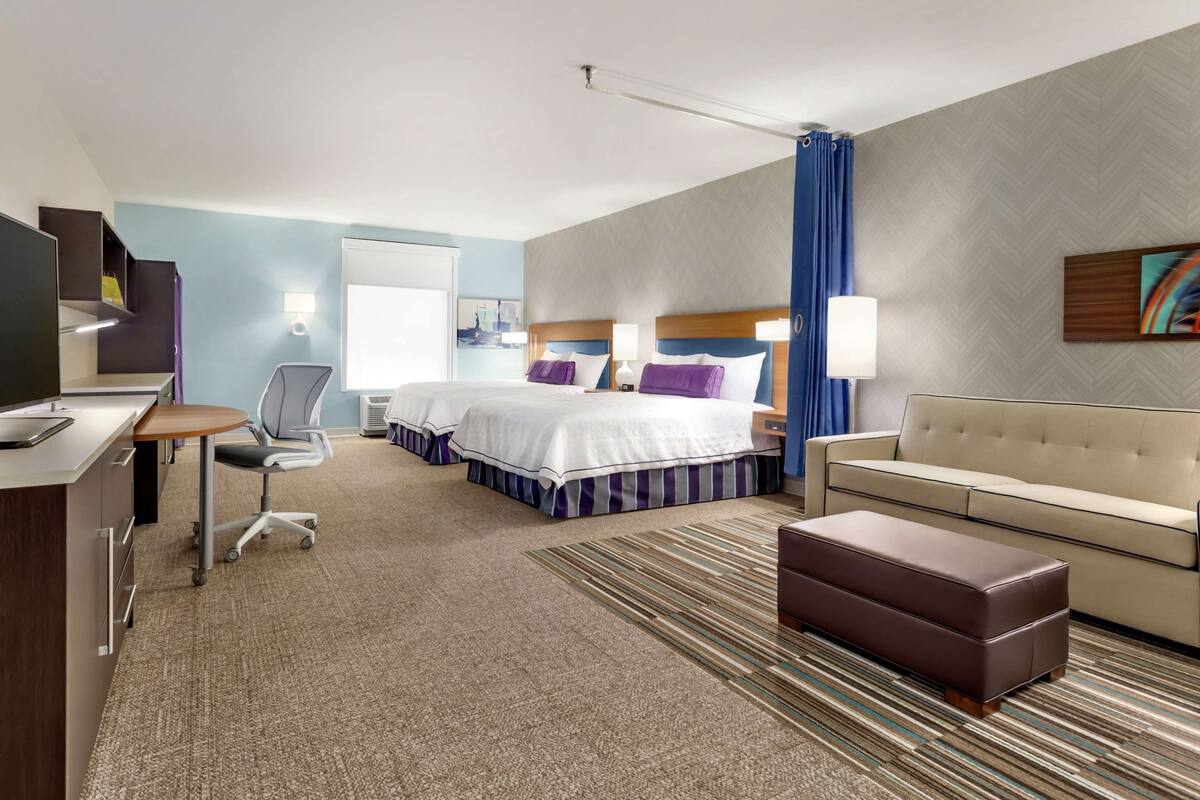 A hotel room with a bed, a desk, a chair, a sofa, and a TV.