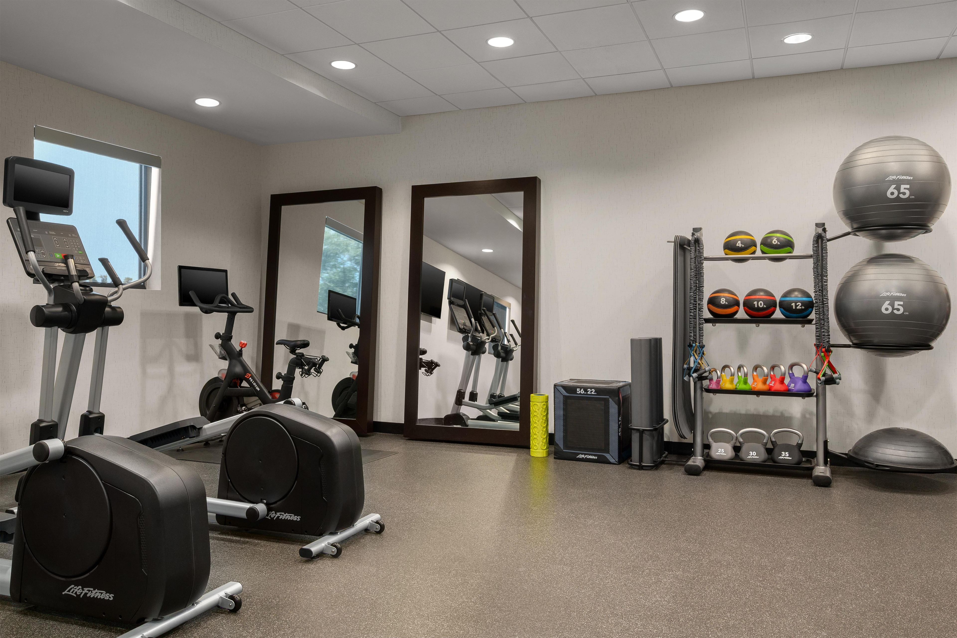 A gym with exercise equipment, mirrors, and a weight rack.