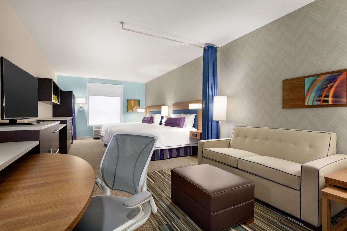 A hotel room with a bed, a sofa, a desk, and a TV.