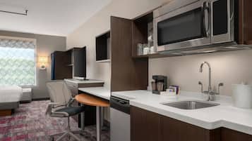 A hotel room with a kitchenette, including a microwave, coffee maker, and sink.