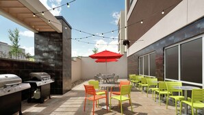 Un patio al aire libre con una parrilla, sillas y mesas, con un paraguas rojo y luces colgantes.