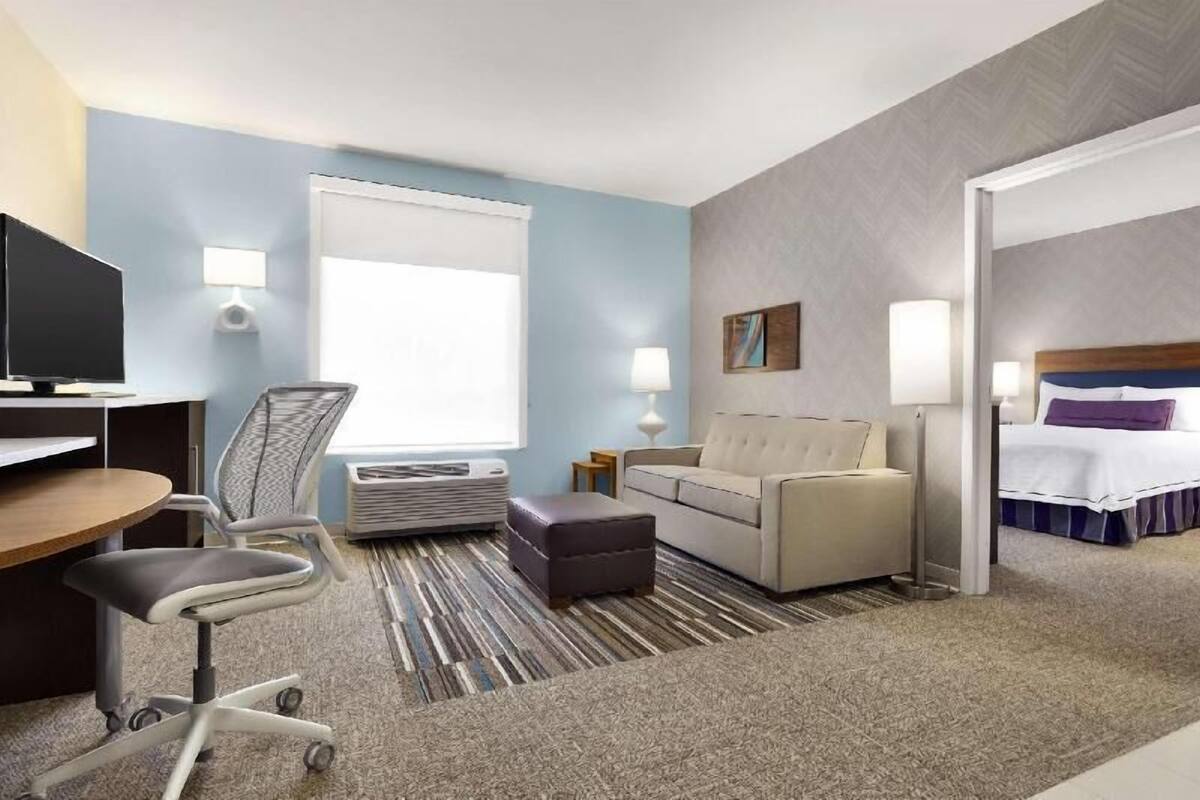 A hotel room with a desk, office chair, sofa, ottoman, and a bed.