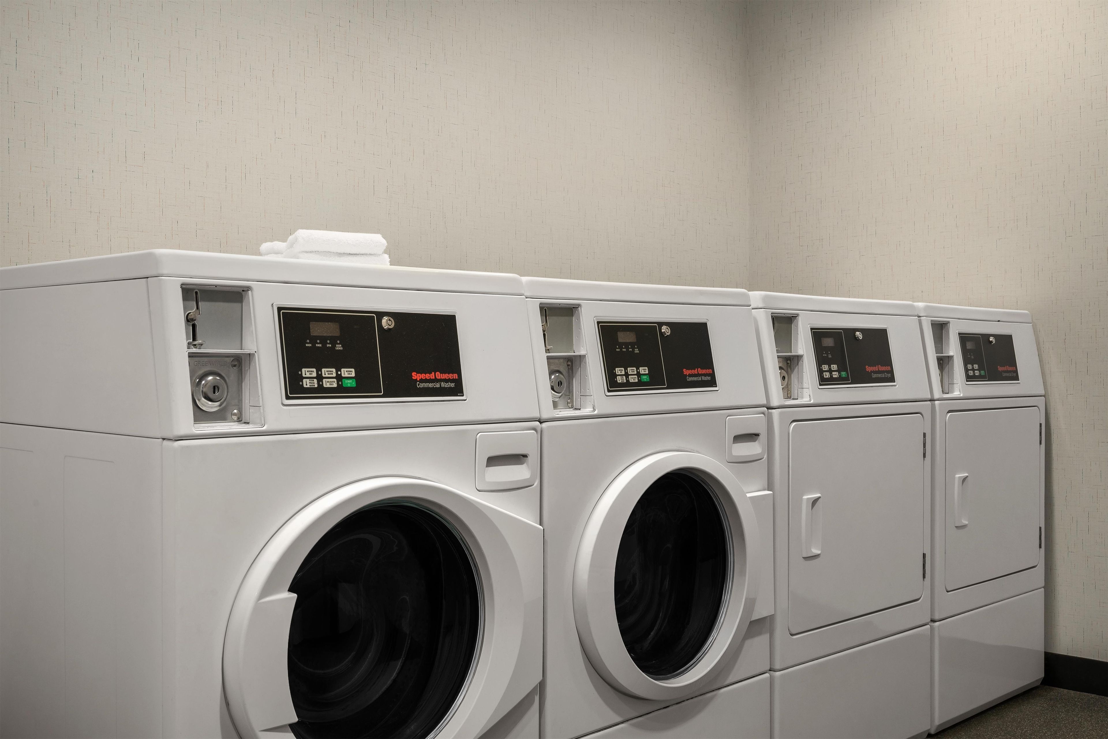 A row of white commercial washers with control panels, in a room with plain walls.