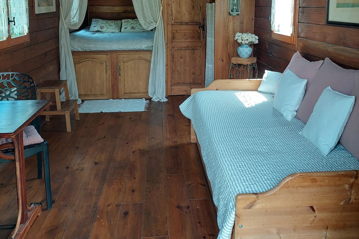 Ein gemütliches Blockhausszimmer mit Holzboden, einem Bett mit blau-weiß karierter Bettdecke, einer Holzbank und einem kleinen Tisch.