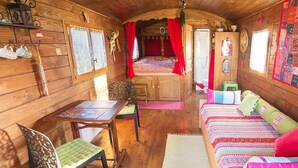 Ein gemütliches Blockhaus-Interieur mit Holzboden, einem Bett mit roten Vorhängen, einem Esstisch mit Stühlen und einem kleinen Hocker.