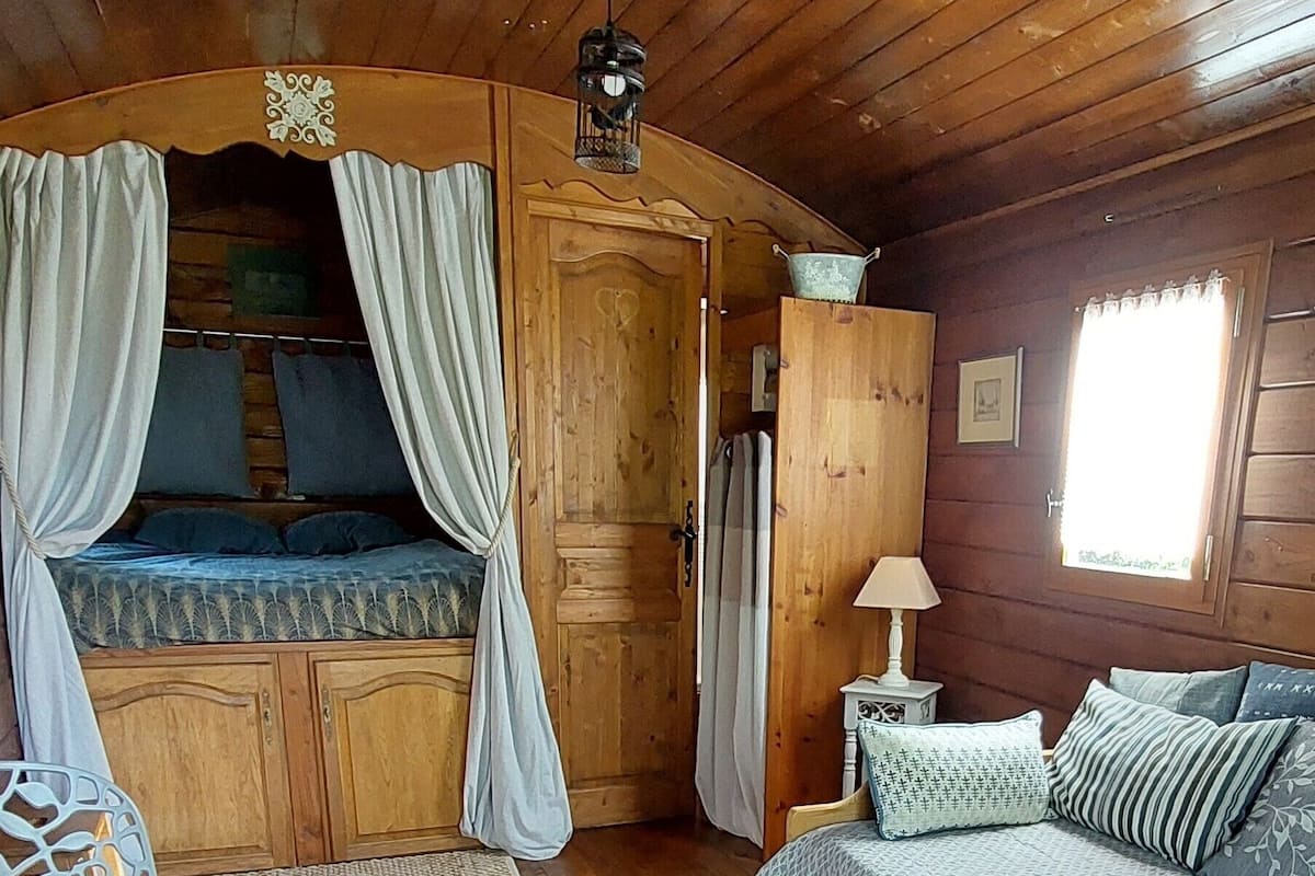 Ein gemütliches Zimmer im Blockhausstil mit einem Bett, einem Sessel, einem kleinen Tisch und einem Fenster.
