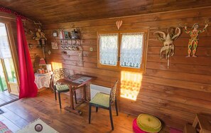 L’intérieur d’un chalet en bois chaleureux et accueillant, avec un coin repas, une table, des chaises, une fenêtre ornée de rideaux en dentelle et divers éléments décoratifs sur les murs.