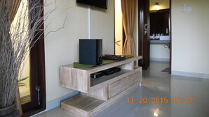 Une chambre d’hôtel avec un meuble de rangement en bois, un téléviseur à écran plat, une plante en pot et une salle de bain visible à travers une porte ouverte.