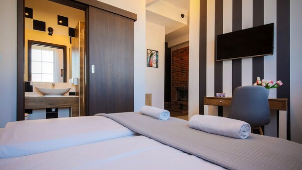 A hotel room with a large bed, a flat-screen TV, a wooden desk, and a fireplace. - Boogie Aparthouse Old Town (Wroclaw)
