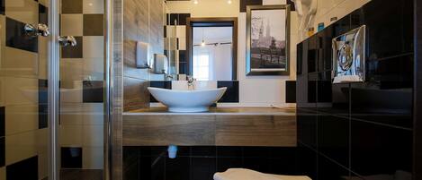 Un baño moderno con cabina de ducha de vidrio, un lavamanos grande de color blanco y pared con azulejos blanco y negro.