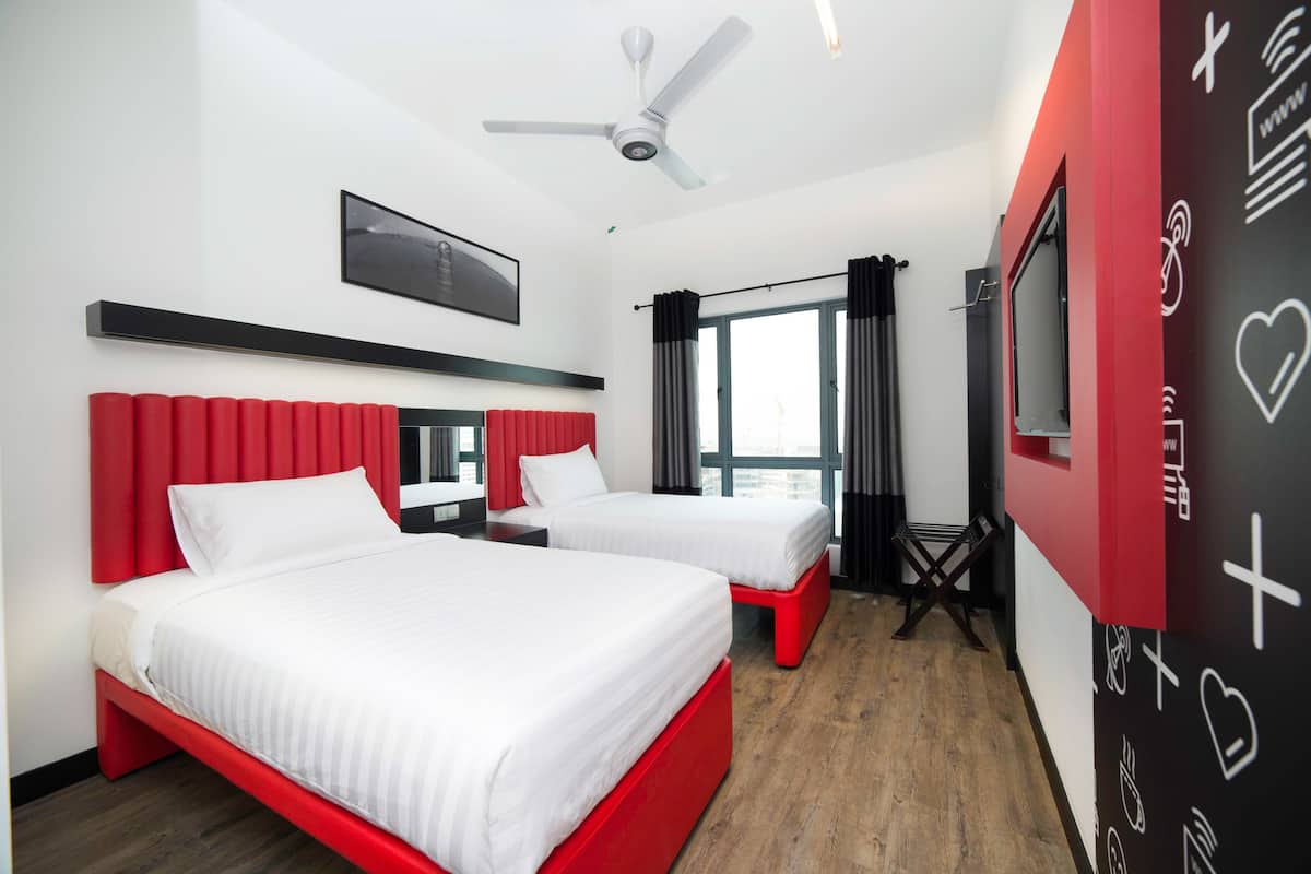 Een hotelkamer met twee bedden, een plafondventilator, een televisie en een groot raam met gordijnen.