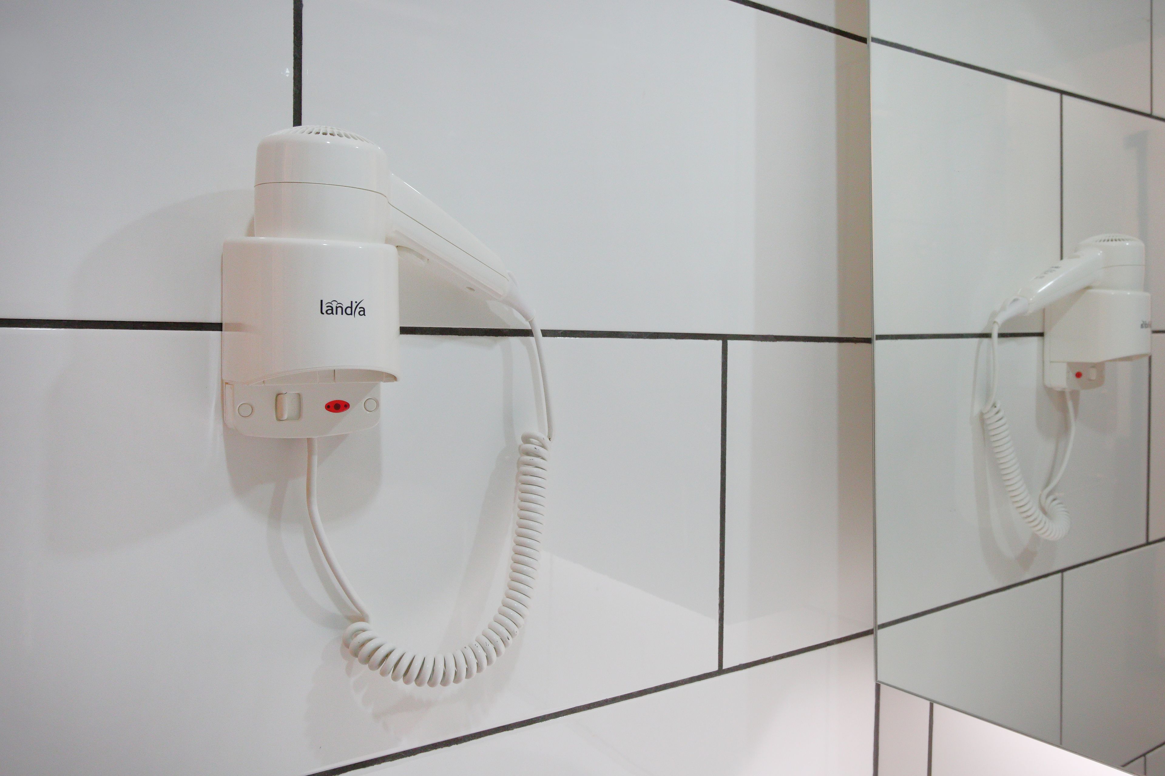 Ein Haartrockner an einer gefliesten Wand in einem Badezimmer.