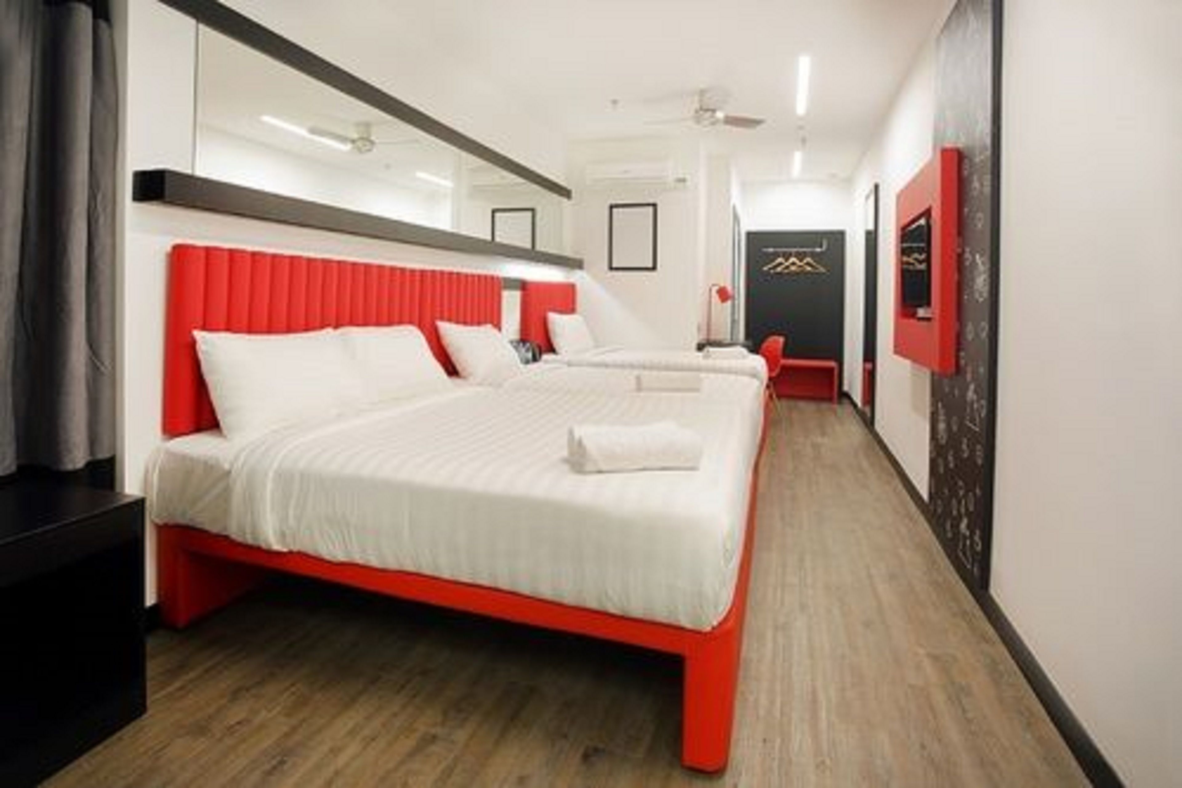A hotel room with a red bed, white bedding, and a wooden floor.