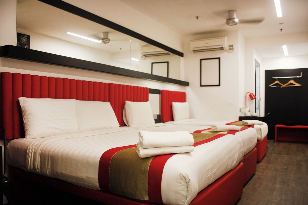 A hotel room with a large bed, red headboard, and a red bench.
