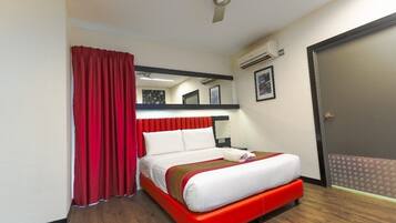 Habitación de hotel con cama, cortinas rojas, ventilador de techo, equipo de aire acondicionado y puerta con felpudo estampado.