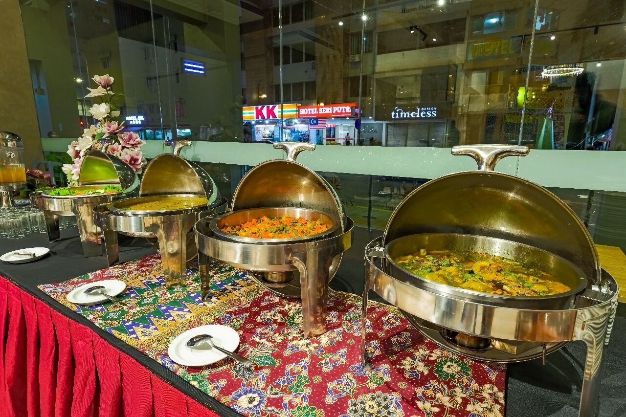 Servicio de comidas tipo buffet con varias estaciones de servicio, mantel estampado y vista al interior del hotel.
