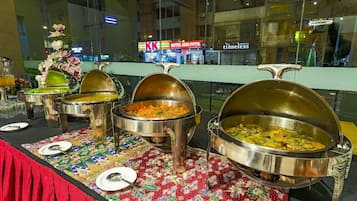 Servicio de comidas tipo buffet con varias estaciones de servicio, mantel estampado y vista al interior del hotel.