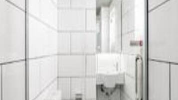 A small, enclosed bathroom with white tiles, a toilet, and a sink.