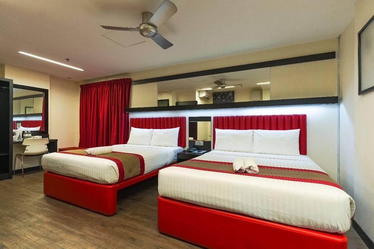 Een hotelkamer met twee bedden, rode gordijnen, een plafondventilator en een spiegel aan de muur.