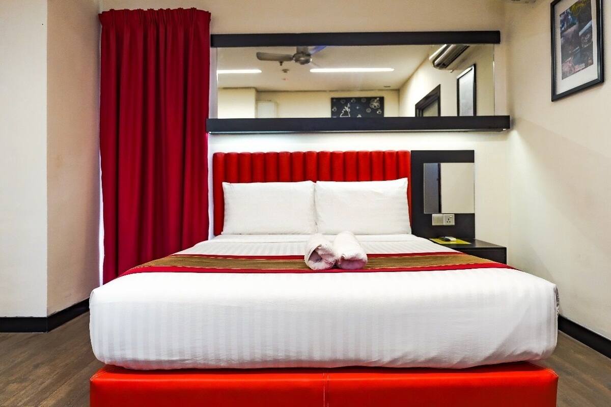 Een hotelkamer met een groot bed, rode gordijnen, een spiegel boven het bed en een rode bank aan het voeteneinde.