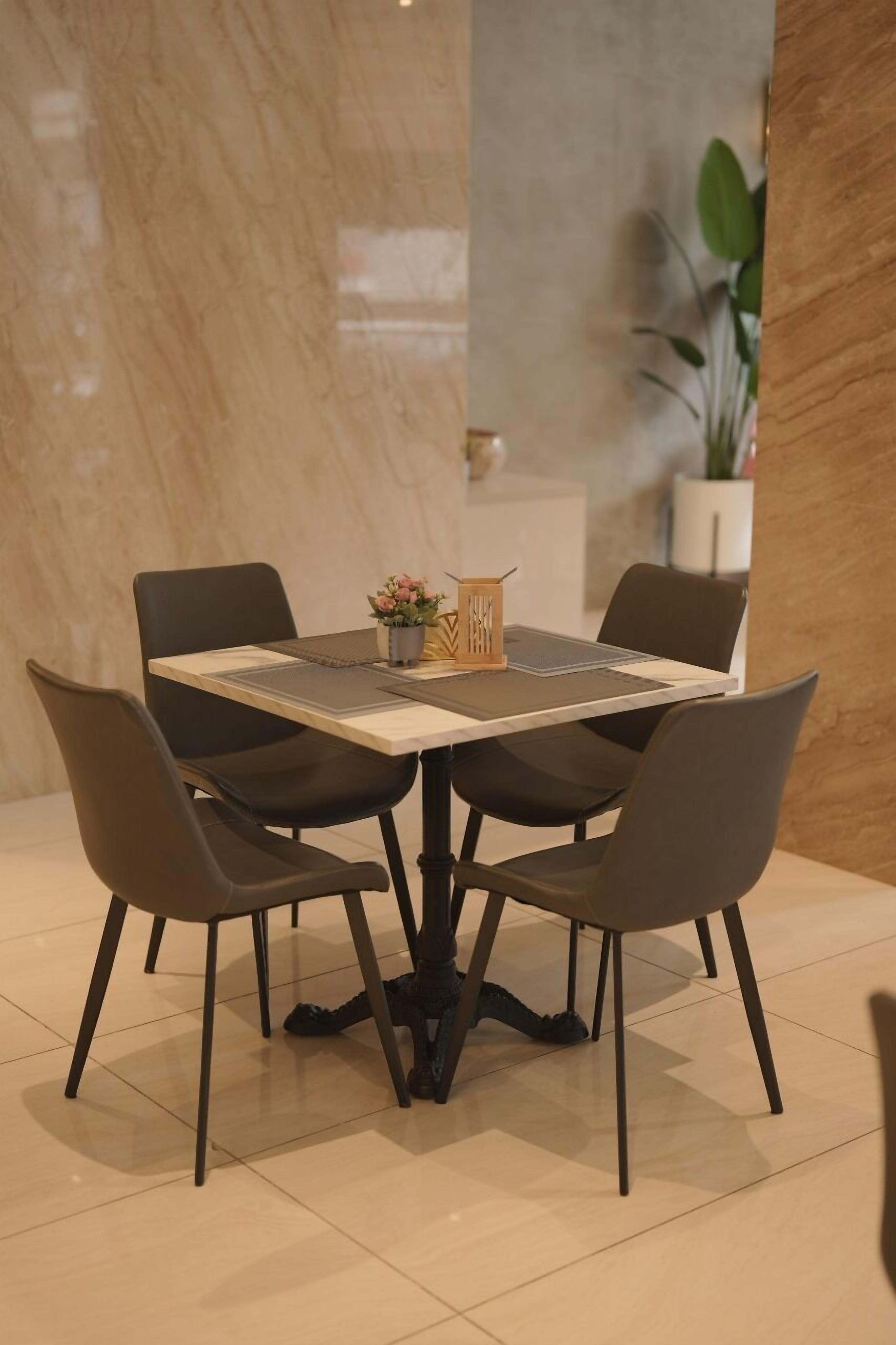 A dining area with a marble wall, a table with four chairs, and a potted plant.
