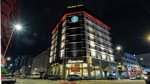 Um hotel de vários andares com uma placa de destaque que diz "Lazdana Hotel" e um restaurante KFC no andar térreo.