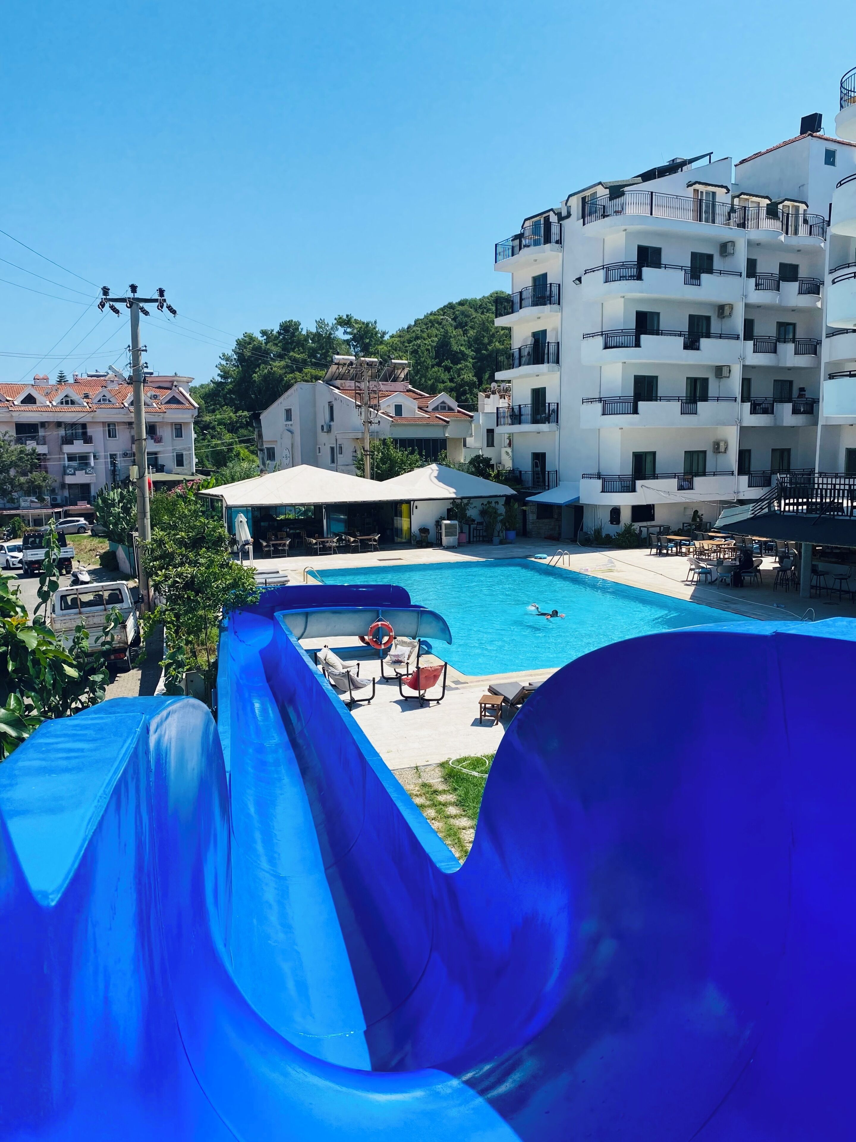 Una piscina con un tobogán azul, rodeada de edificios y un cielo despejado.