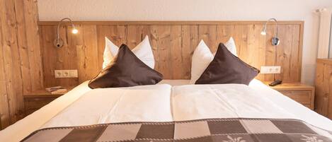 A hotel room with a wooden headboard, two bedside tables, a bed with white bedding and a patterned throw, and two wall-mounted lamps.