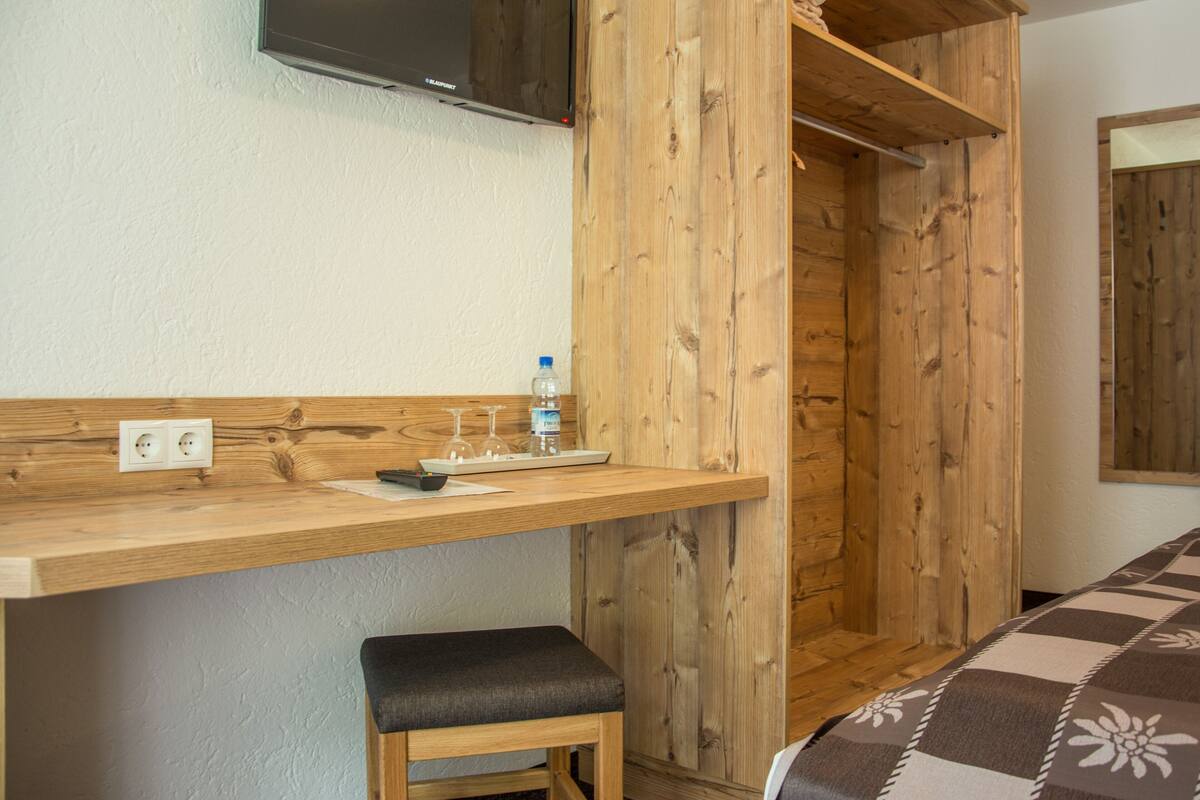Um quarto de madeira com uma escrivaninha, banco e espelho.