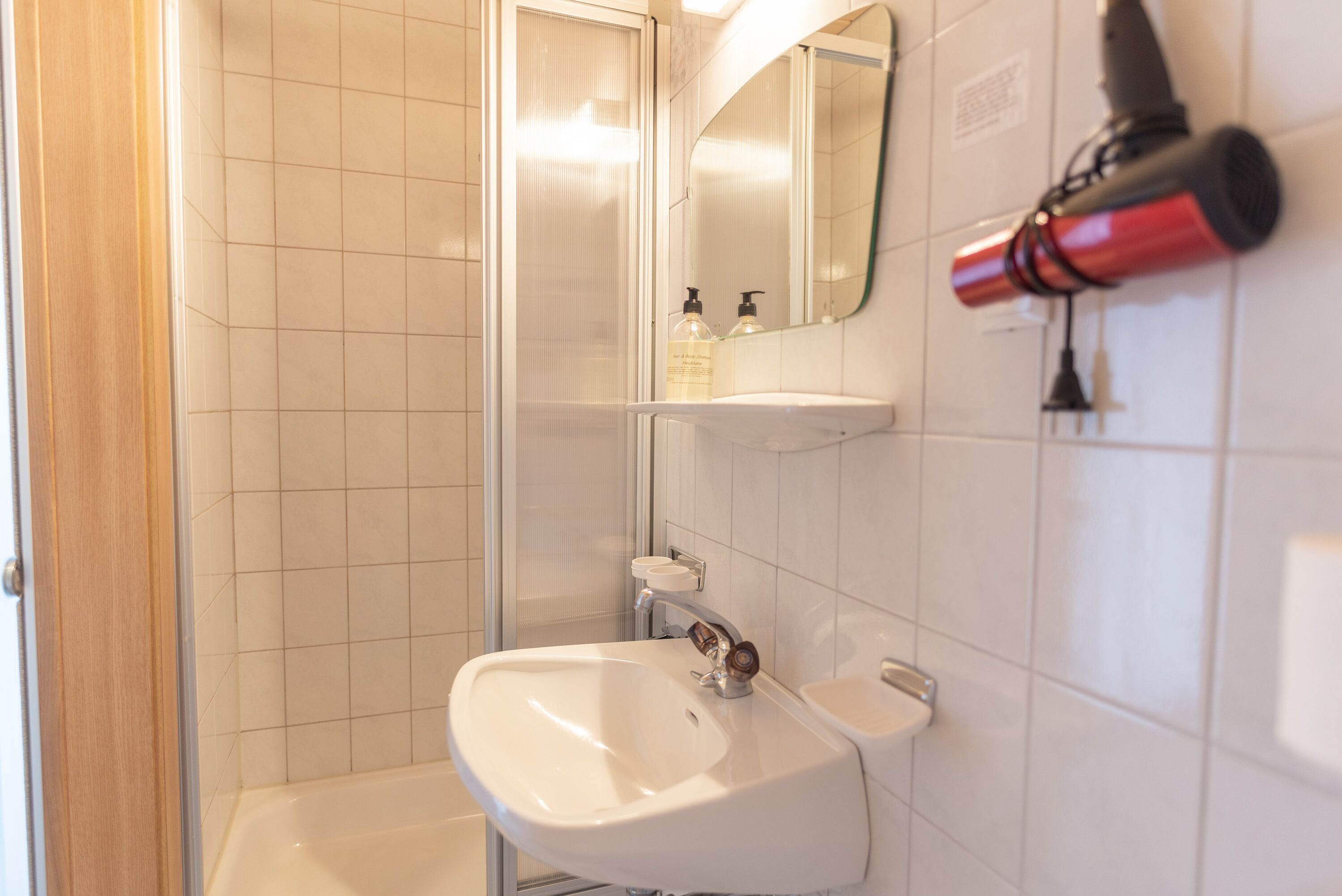 Een badkamer met een witte wastafel, een spiegel en een föhn bevestigd aan de muur.