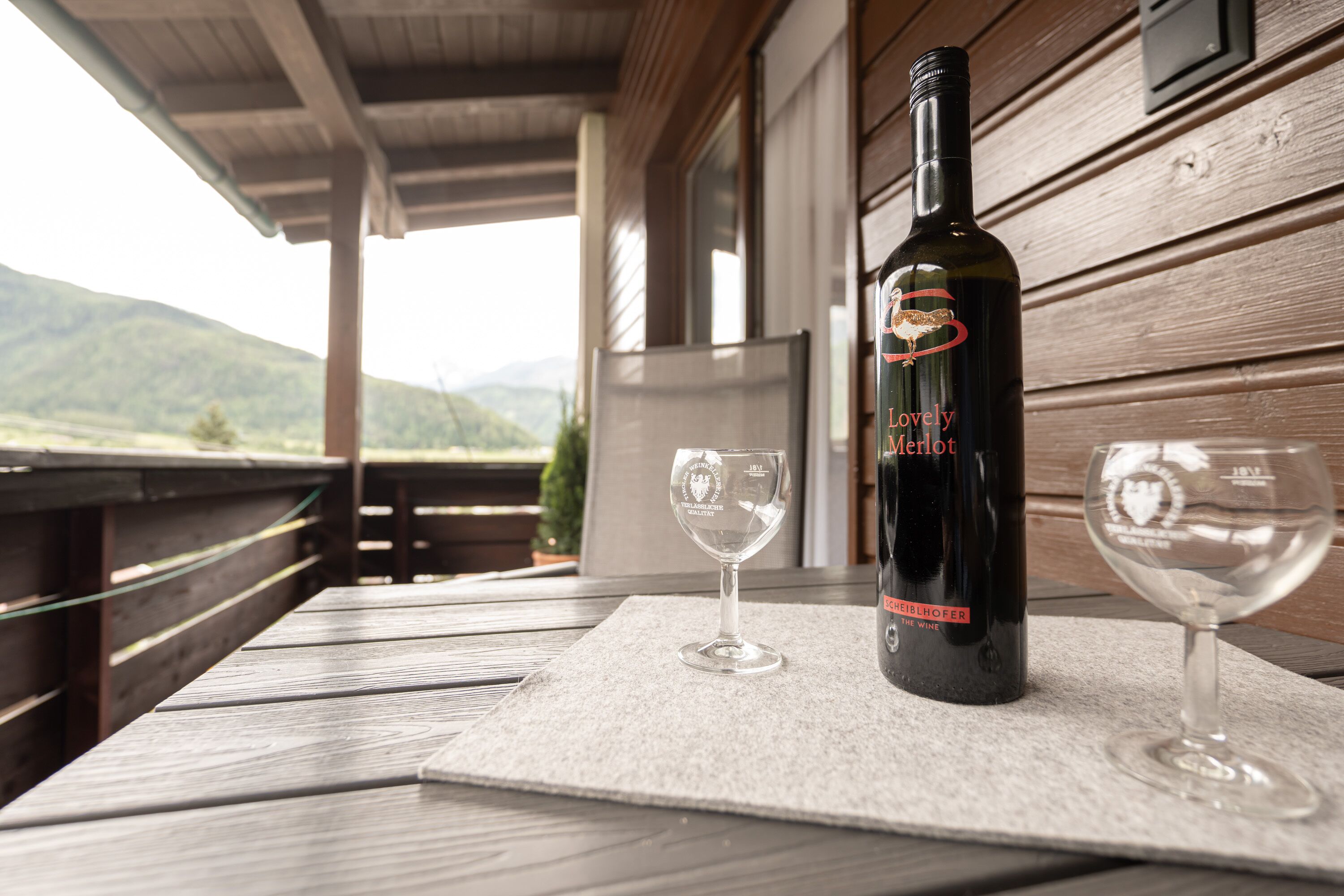 Una botella de vino y dos copas sobre una mesa de madera, con vistas a las montañas.