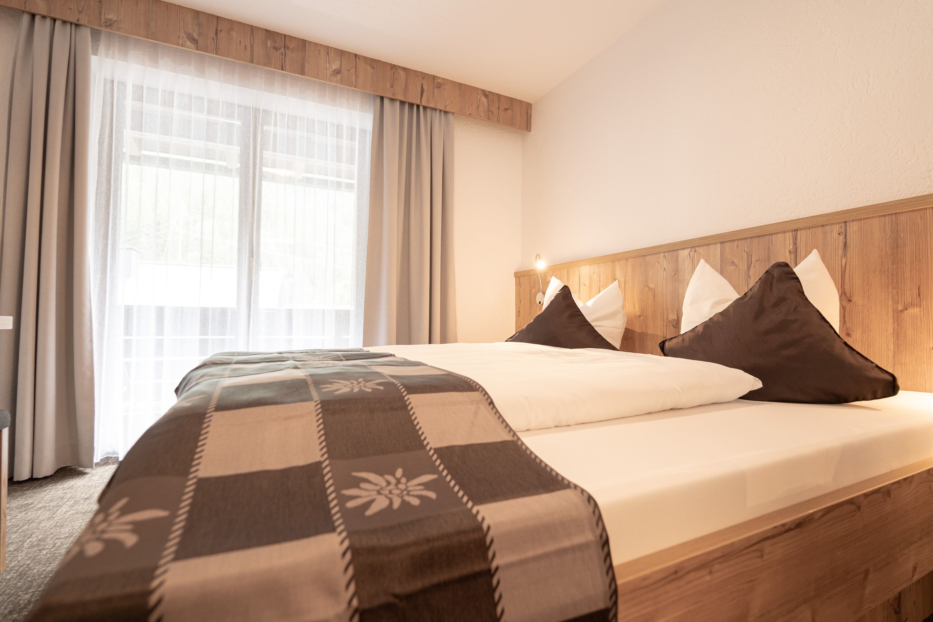 A hotel room with a large bed, wooden headboard, and a window with curtains.
