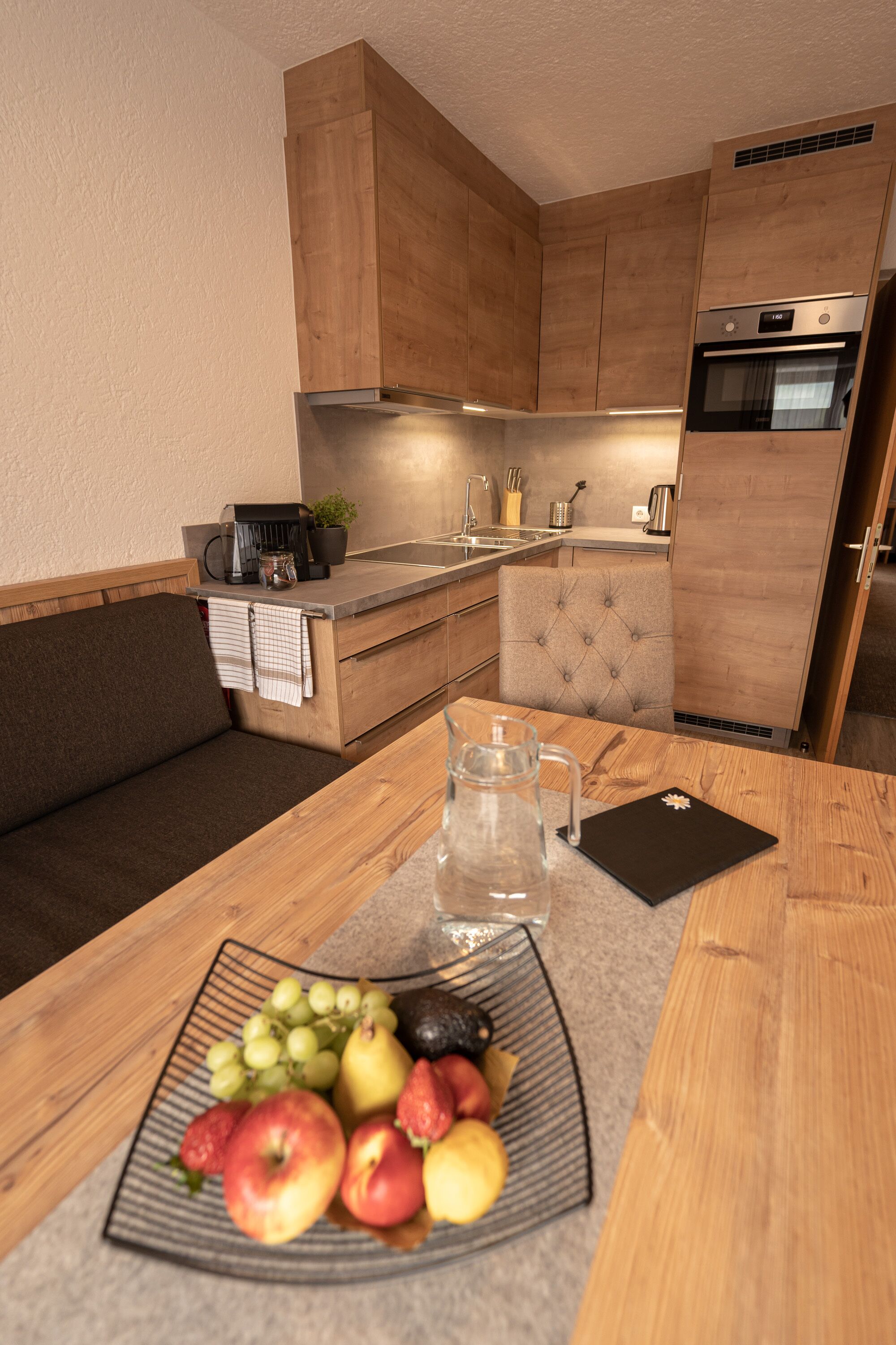 Eine kompakte Küche mit Holzausstattung, einem eingebauten Backofen und einer Essecke mit Tisch für zwei Personen.