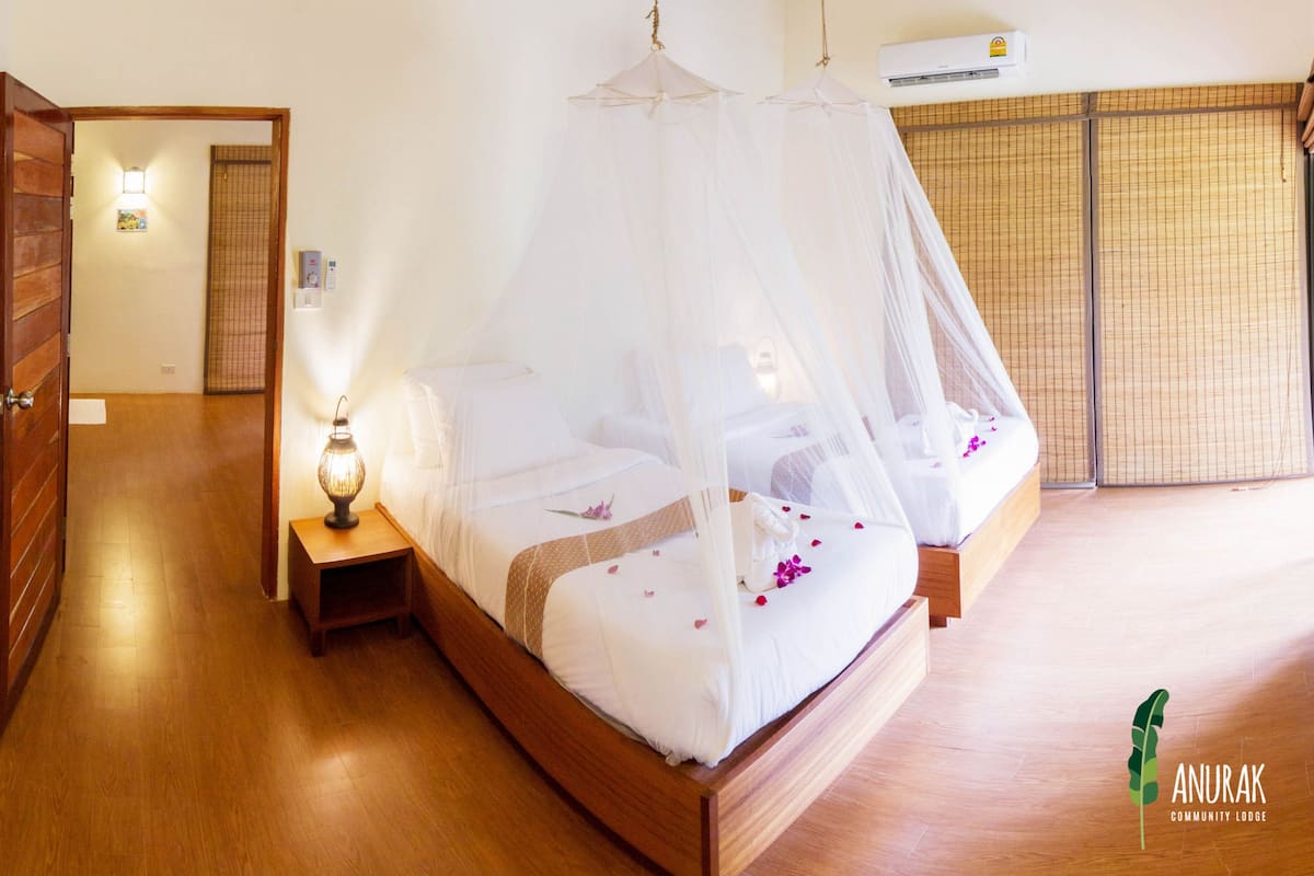 A room with a bed under a mosquito net, a ceiling fan, and a nightstand with a lamp.