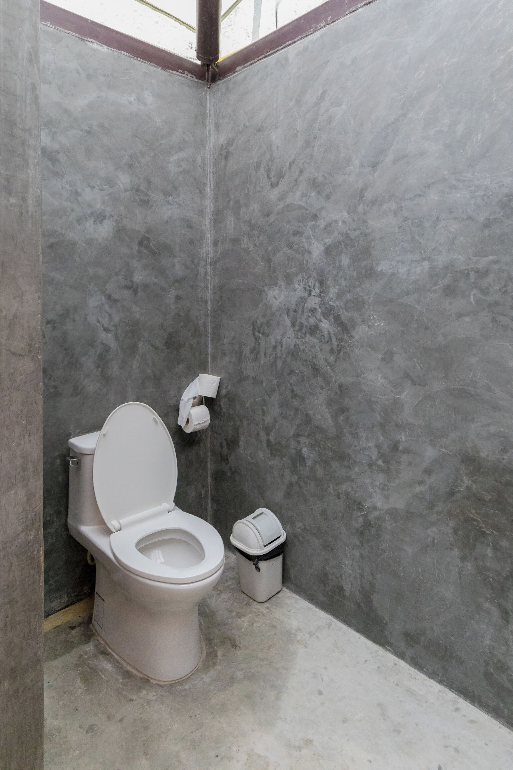 A bathroom with a white toilet, a trash bin, and a towel dispenser on the wall.