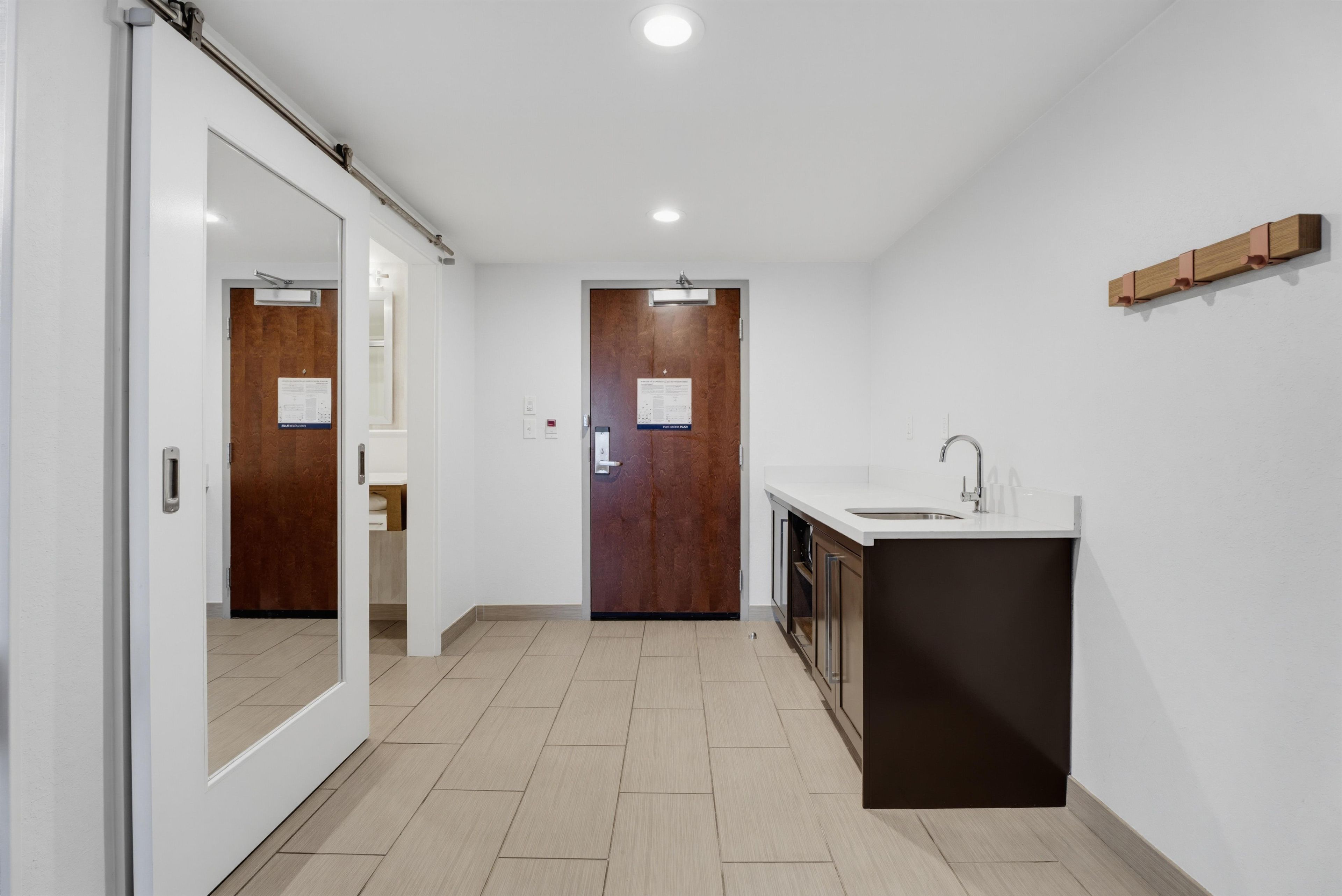 A modern kitchen with a built-in sink and cabinets, a wooden door, and a hallway leading to another room.