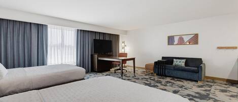 Een hotelkamer met twee bedden, een bureau, een televisie, een bank en een schilderij aan de muur.
