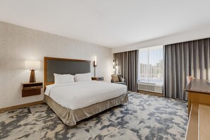A hotel room with a large bed, a desk, a chair, a nightstand, and a window with curtains. - Hampton Inn by Hilton Detroit Dearborn (Dearborn)