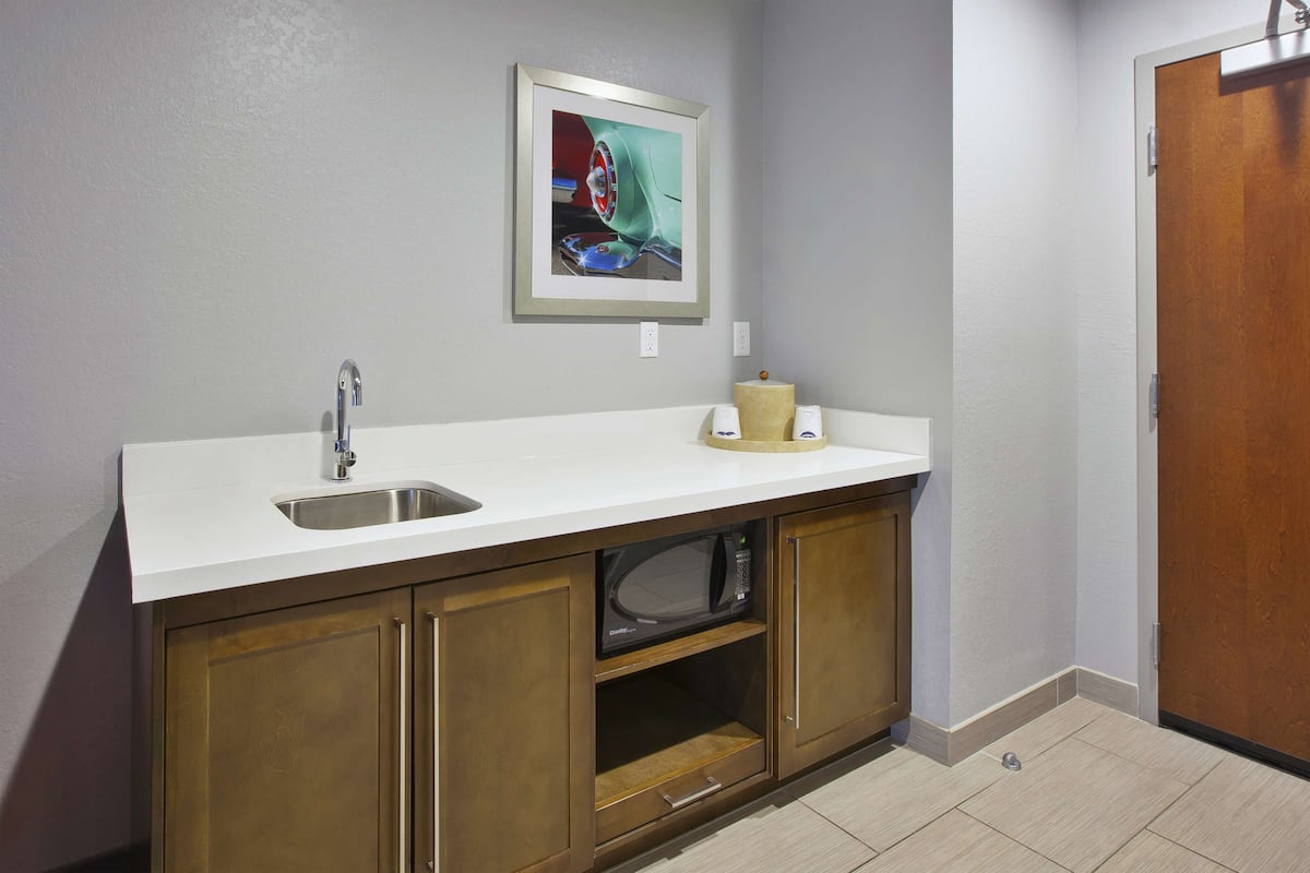 A kitchen with a white countertop, a stainless steel sink, a microwave, and wooden cabinets.