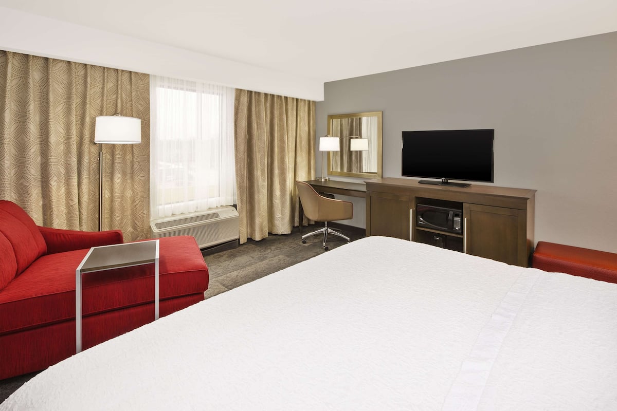 A hotel room with a large bed, a desk with a chair, a television, and a red sofa.