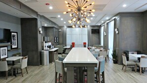 A modern dining area with a long table, multiple chairs, a unique light fixture, and a bar area with a counter and stools.